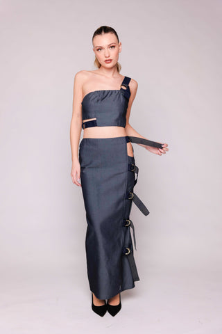 Woman wearing a dark gray one-shoulder outfit with long skirt on a light gray background