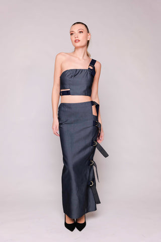 Woman wearing a dark gray one-shoulder top and long skirt on a light gray background