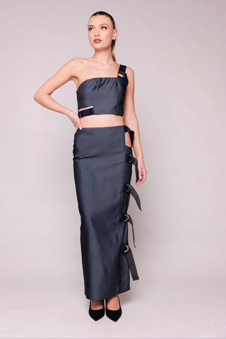 Woman wearing a dark blue one-shoulder top and long skirt against a plain background