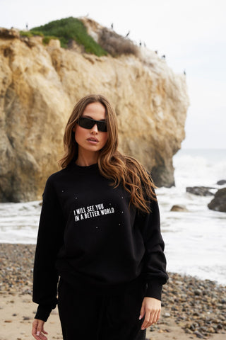 Model wearing Back Bone Society's In A Better World Hoodie on California beach, part of unisex Streetwear collection