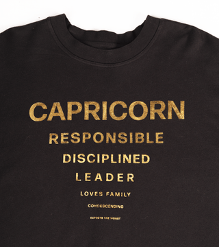 black crewneck with text in gold reflective foil "Capricorn, Responsible, Disciplined, Leader, Loves Family, Condescending, Expects the Worst."